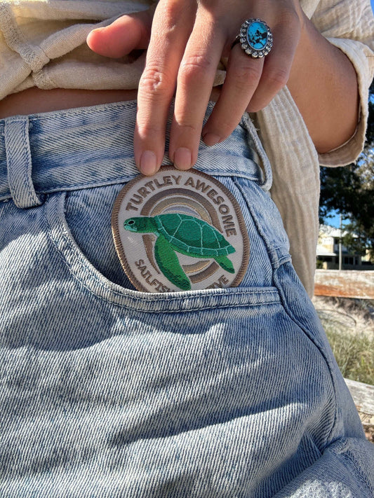 Embroidered iron on patch with green turtle design on denim pocket