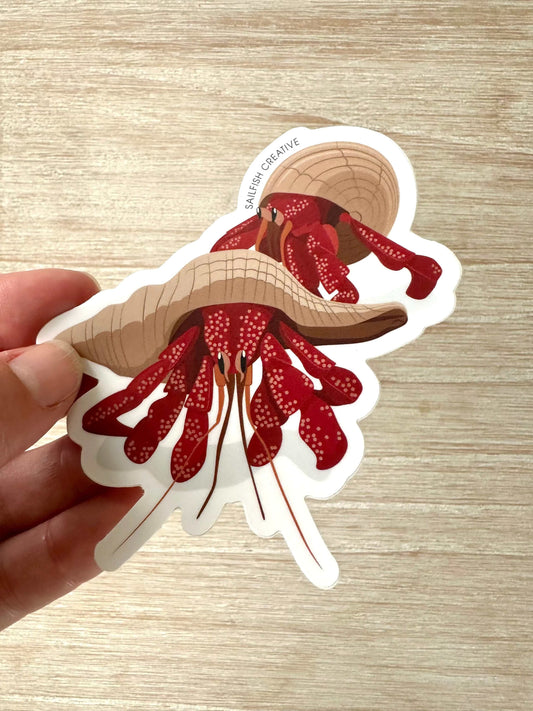 Hand holding a 90mm Strawberry Crab sticker made of permanent polymeric vinyl with matte laminate on a wooden surface