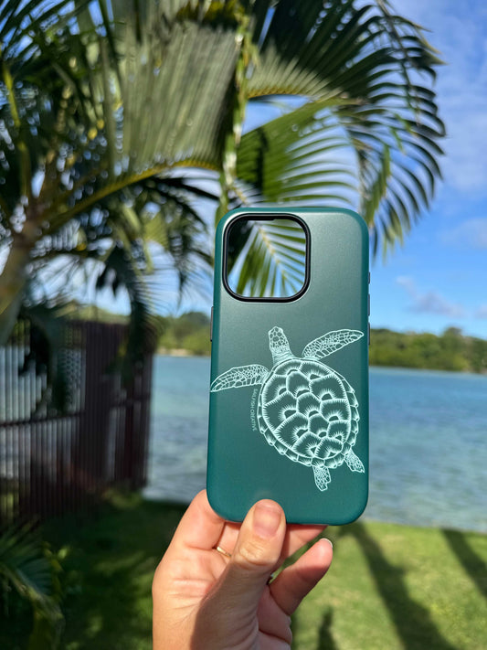 Emerald green iPhone phone case with white turtle outline design held outdoors near palm tree and water background