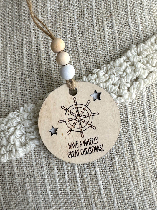 Wooden Christmas decoration with ships wheel design and "Have a wheely great Christmas" text on plywood bauble with jute string and beads
