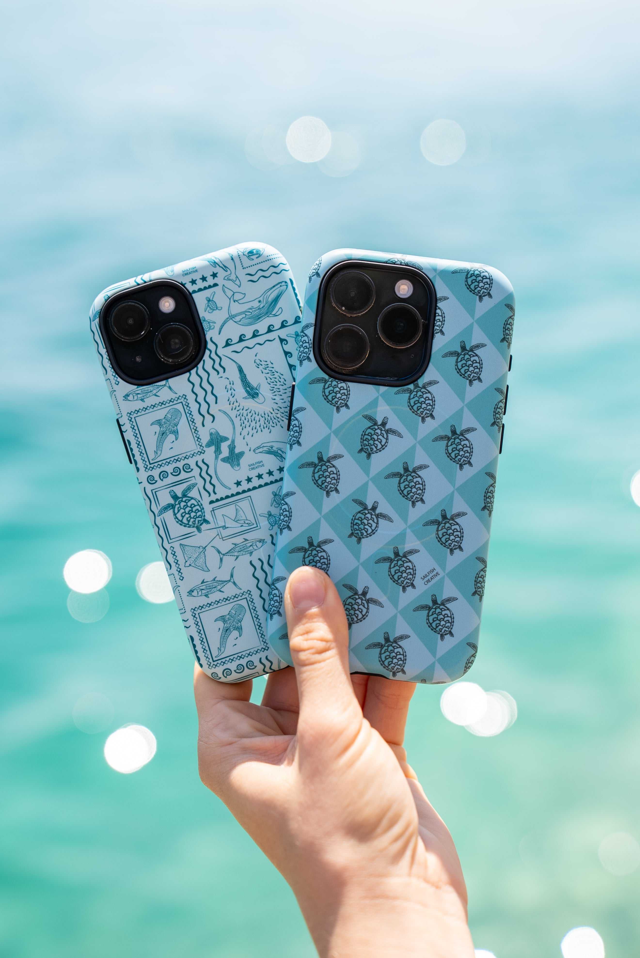 Two teal iPhone phone cases with marine animal prints held against a blurred ocean background