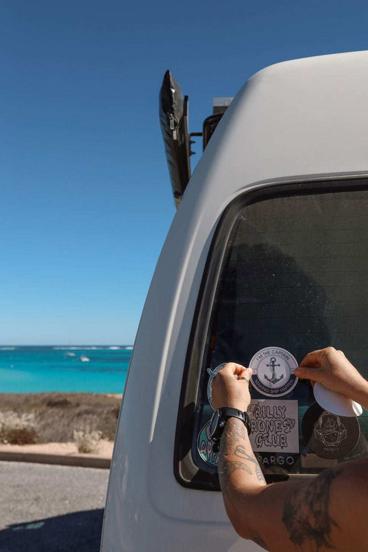 Person applying Anchor and Chain sticker on vehicle window with ocean in background