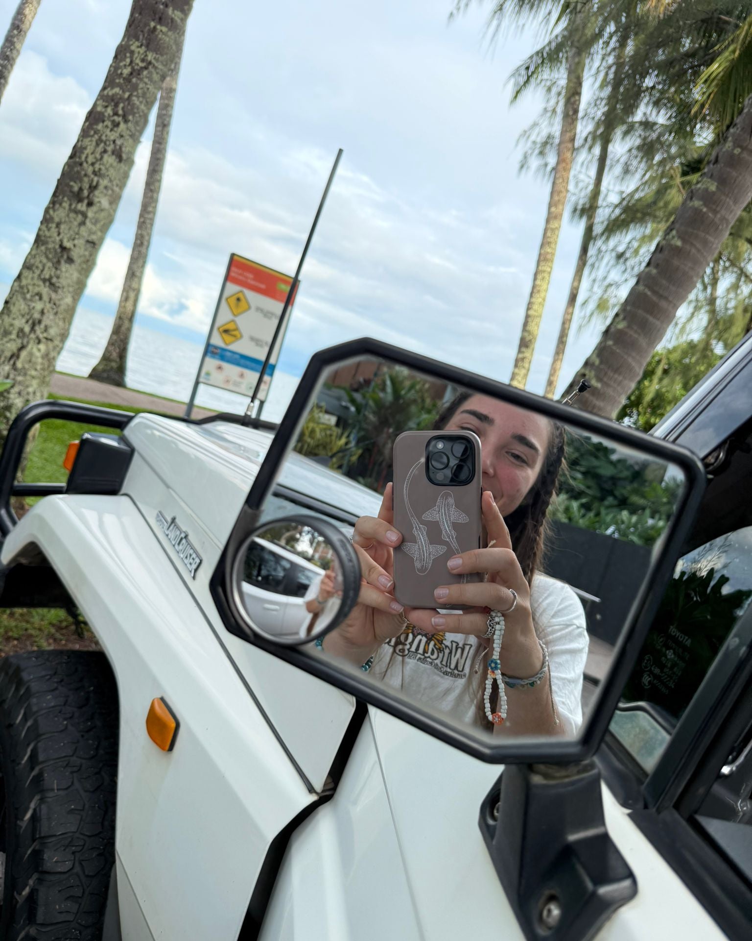 Sheree taking a mirror selfie in a vehicle with leopard shark phone case palm trees and palm beach queensland in the background.