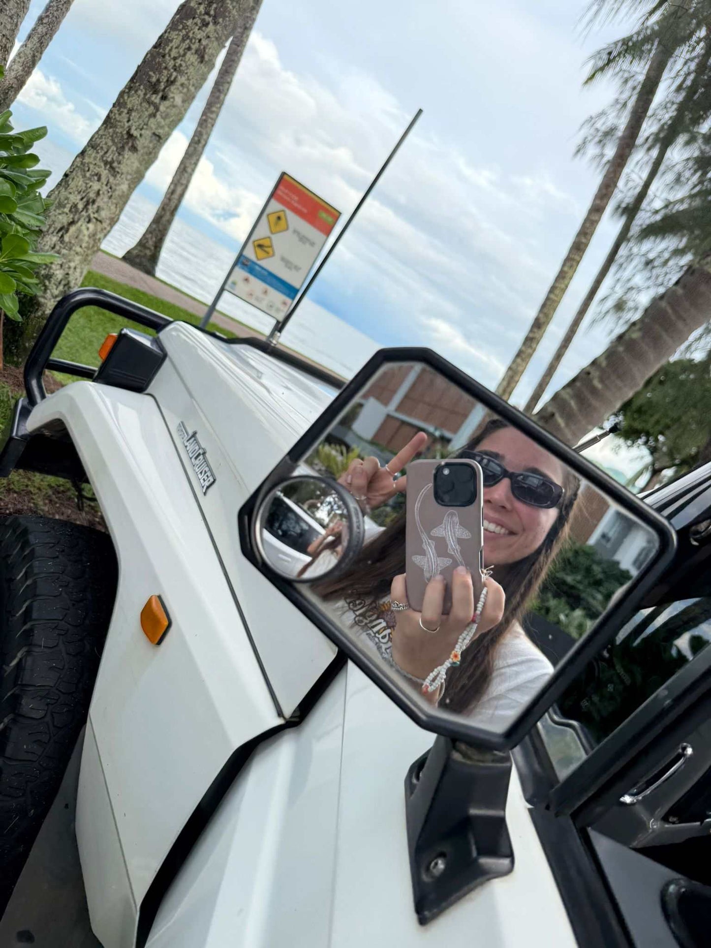 iPhone phone case with leopard sharks outline design held in hand reflected in car side mirror outdoors