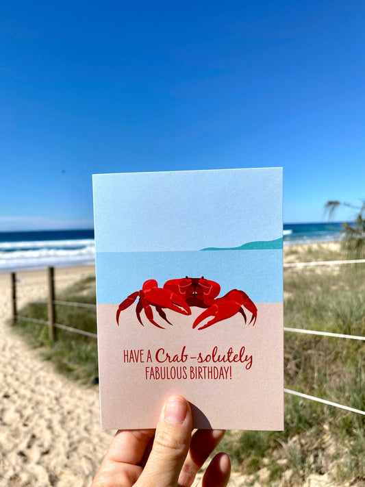 Birthday card featuring a red crab illustration with birthday message held at the beach background