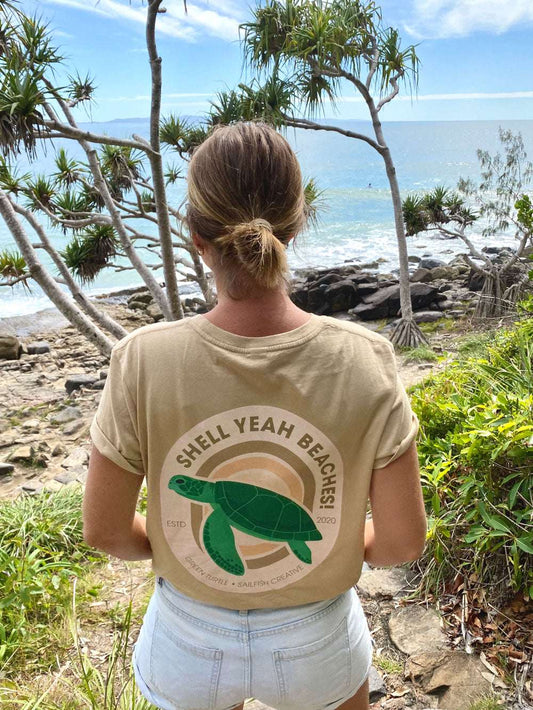 Woman wearing Shell Yeah Beaches t-shirt with green turtle design by the beach