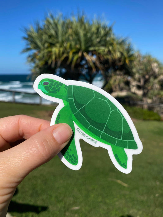 Green Turtle sticker on permanent vinyl held outdoors with ocean and palm trees background