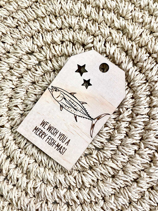 Wooden Christmas swing tag with tuna fish design and Merry Fish-Mas message on textured surface