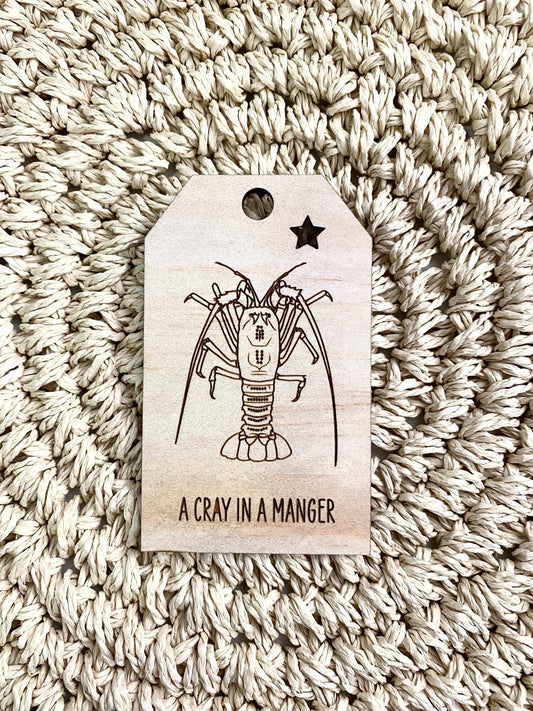 Wooden Christmas swing tag with etched rock lobster crayfish and "A Cray in a Manger" text on plywood background