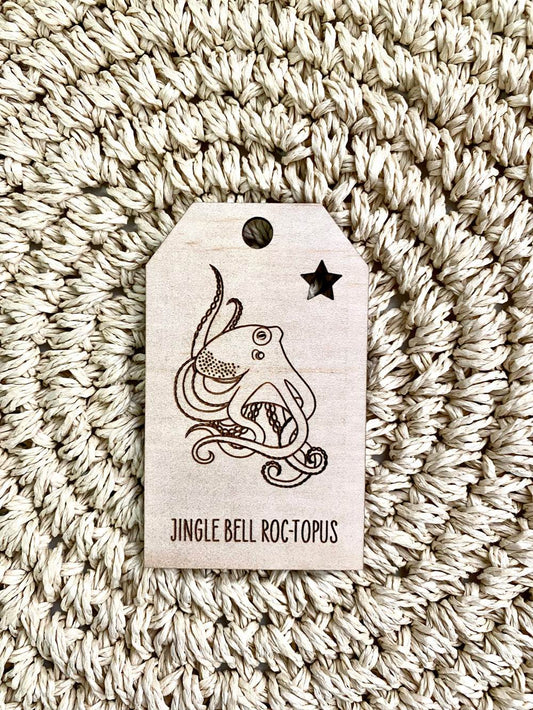 Wooden Christmas swing tag with octopus design and "Jingle Bell Roc-topus" text on plywood surface.