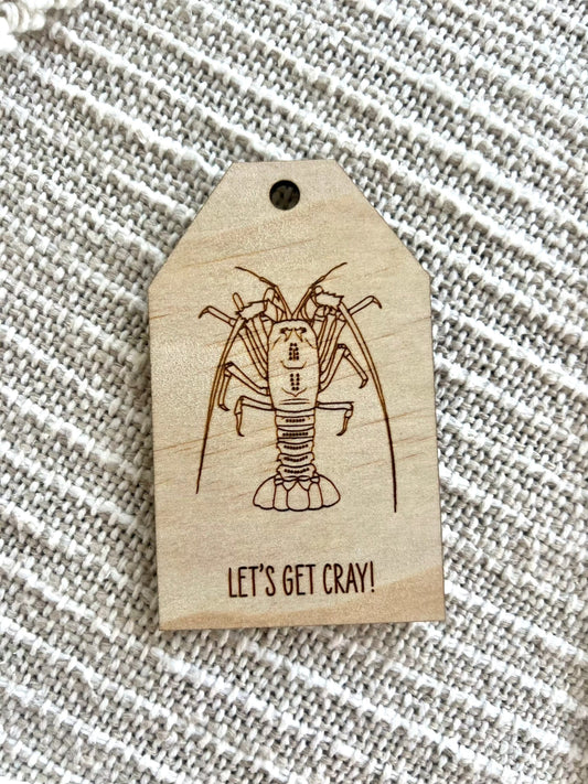 Wooden gift tag with etched crayfish design and "Let's Get Cray!" text on plywood background