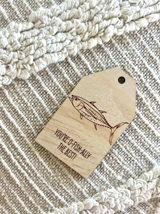 Wooden gift tag with etched tuna fish design and "You're o-fish-ally the best" text on plywood background