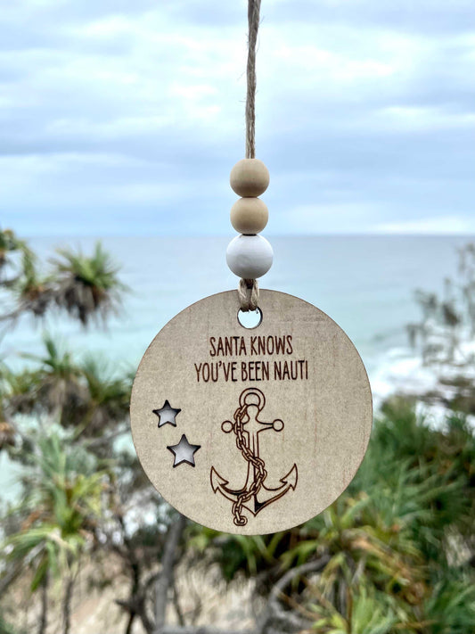 Wooden Christmas decoration nautical anchor with chain and text hanging on jute string by the sea