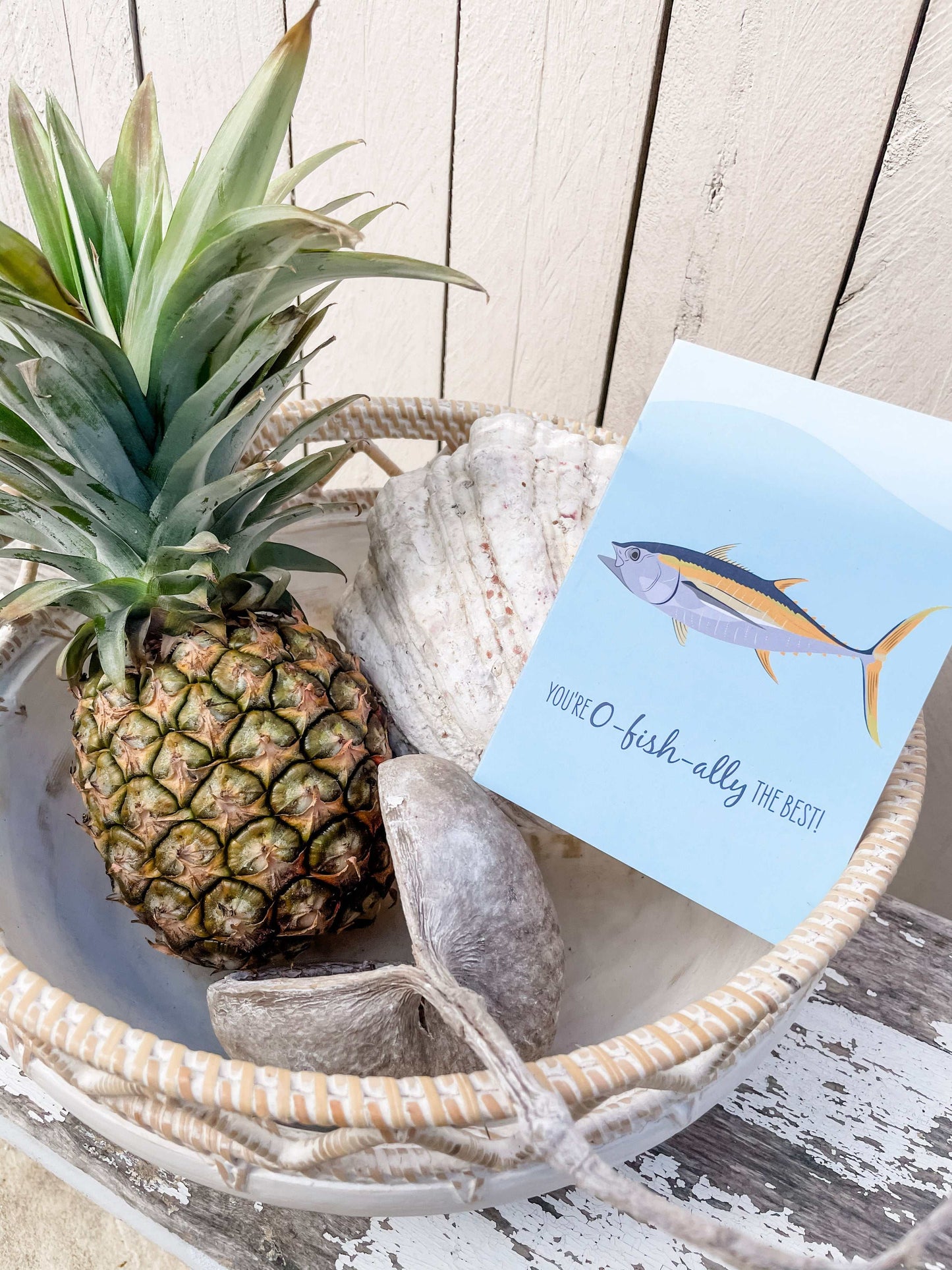 Greeting card with tuna fish illustration beside pineapple and seashells in a basket