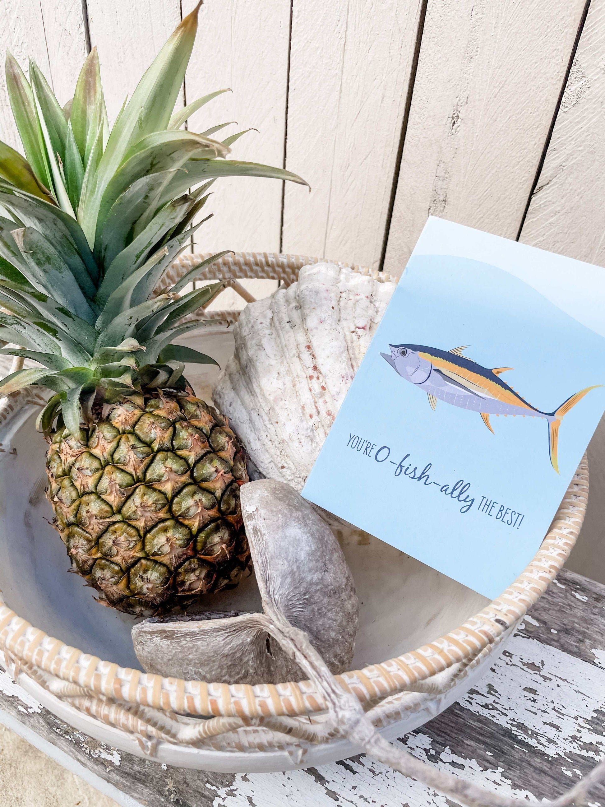 Greeting card with tuna fish illustration beside pineapple and seashells in a basket