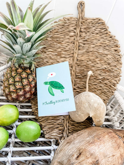 Green Turtle Lovers Card with ocean-themed love message and envelope on woven leaf tray with tropical fruits