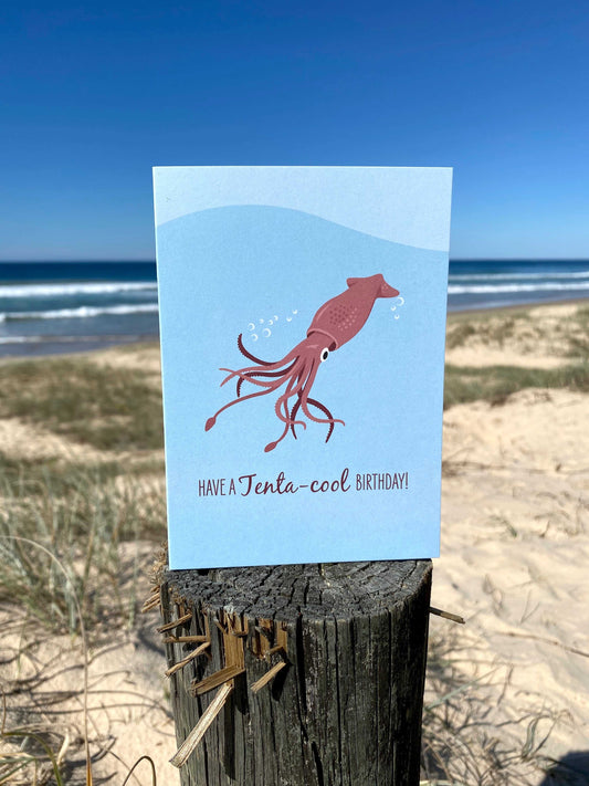 Birthday card with arrow squid illustration and pun text "Have a Tenta-cool Birthday" on beach background