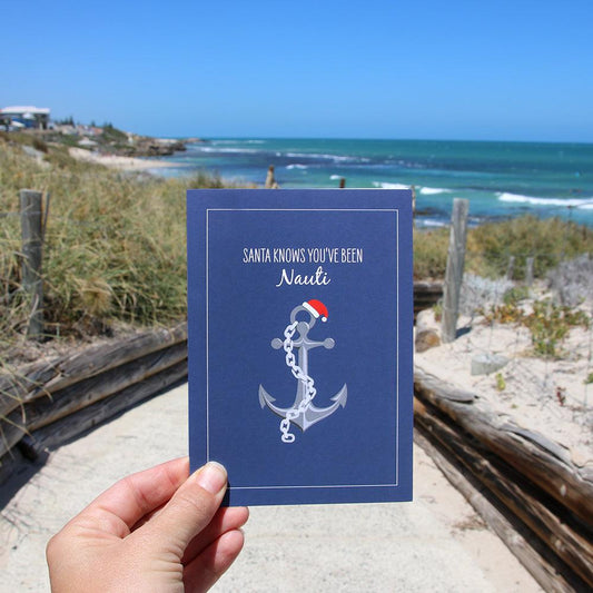 Christmas card with nautical anchor design and festive Santa hat, ocean background.
